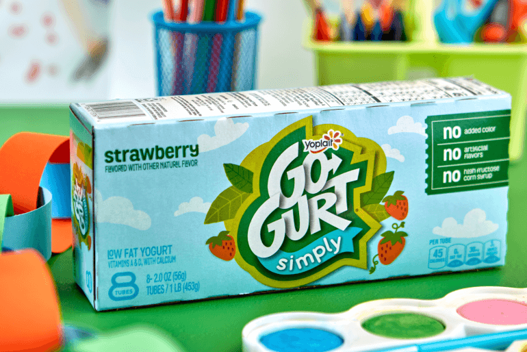 A box of strawberry Simply Go-GURT tubes sitting on a table beside some paint and a paper chain.